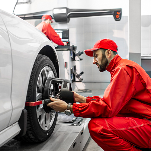 A mechanic dressed in red fixing the vehicle's wheel alignment.